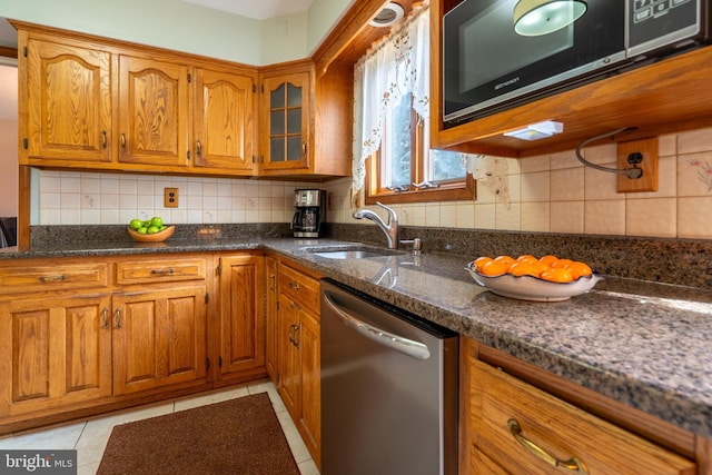 kitchen featuring light tile patterned floors, a sink, decorative backsplash, appliances with stainless steel finishes, and brown cabinets