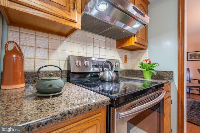 kitchen with under cabinet range hood, tasteful backsplash, stainless steel electric stove, and brown cabinetry