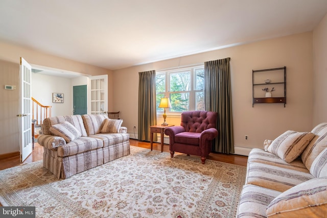 living room featuring a baseboard heating unit, baseboards, wood finished floors, and stairway