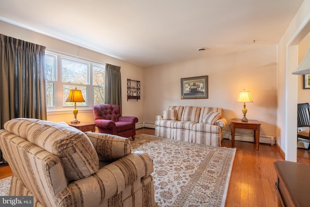 living area with a baseboard heating unit, wood finished floors, baseboards, and baseboard heating