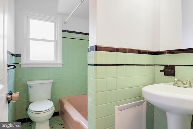 bathroom with a wainscoted wall, toilet, tile walls, and a sink