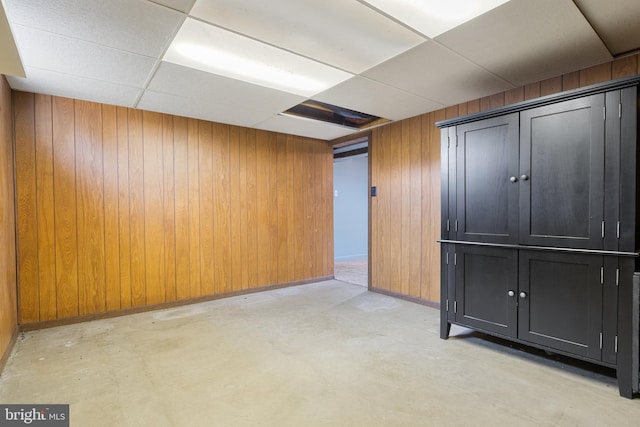 finished basement featuring baseboards, a paneled ceiling, and wooden walls