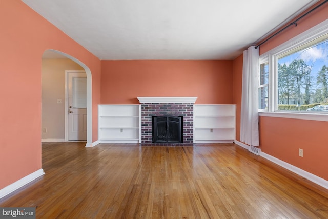 unfurnished living room with visible vents, a brick fireplace, baseboards, wood finished floors, and arched walkways