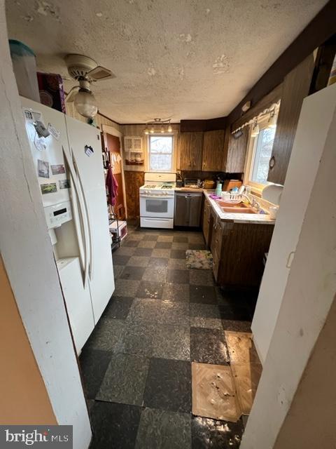 kitchen with a sink, white appliances, plenty of natural light, and dark floors