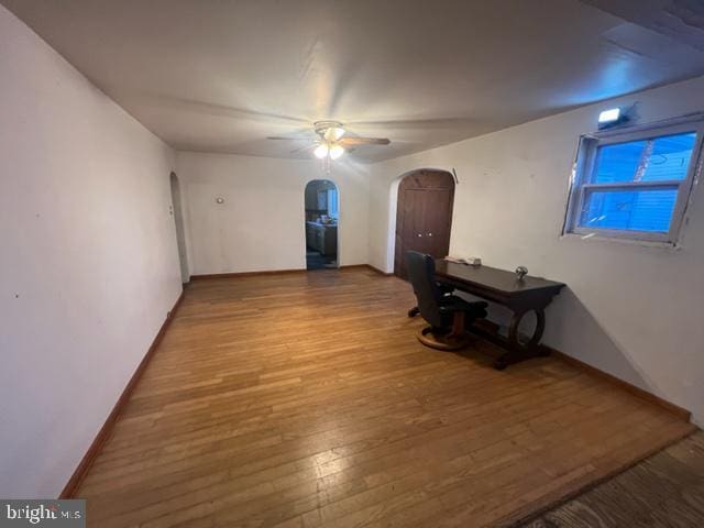 unfurnished room featuring baseboards, arched walkways, wood finished floors, and a ceiling fan