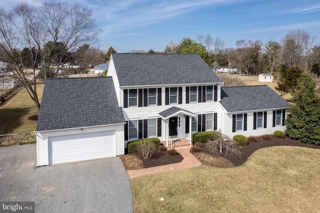 colonial home with aphalt driveway, roof with shingles, a front lawn, and fence