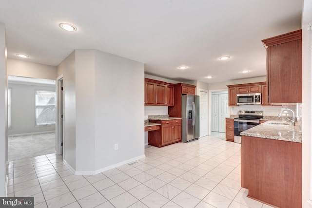 kitchen with a sink, baseboards, light stone countertops, and appliances with stainless steel finishes