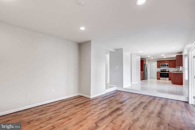 unfurnished living room featuring a sink, light wood-type flooring, baseboards, and recessed lighting