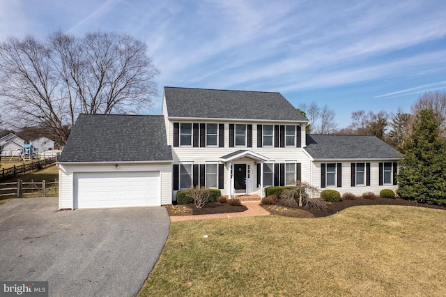 colonial home featuring a shingled roof, a front lawn, fence, a garage, and driveway