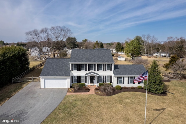 colonial inspired home with an attached garage, a front lawn, fence, roof with shingles, and driveway