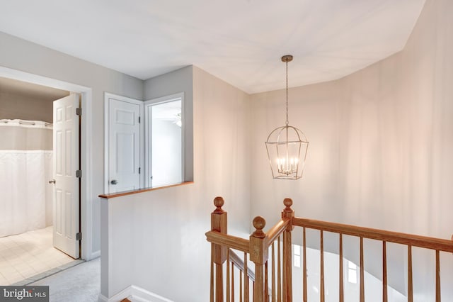 hall featuring a notable chandelier, an upstairs landing, and baseboards