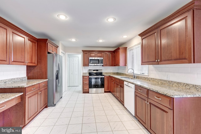 kitchen with a sink, stainless steel appliances, light stone countertops, and decorative backsplash