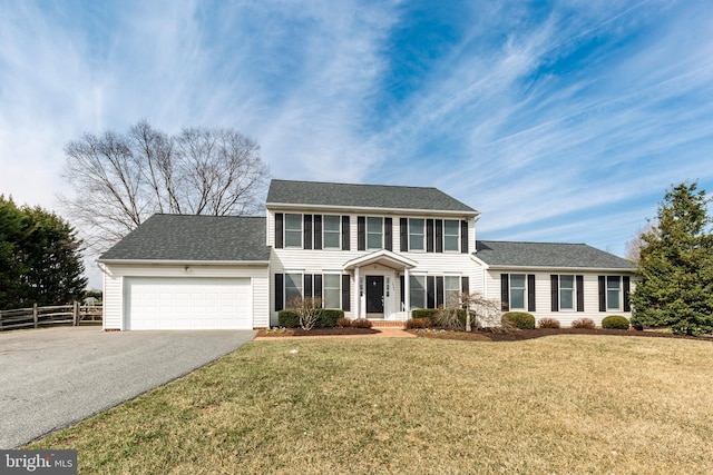 colonial house with aphalt driveway, an attached garage, a front lawn, and fence