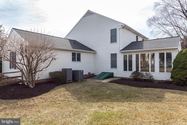 back of property featuring central AC unit, a lawn, and roof with shingles