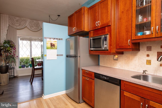 kitchen with light wood-type flooring, light countertops, decorative backsplash, appliances with stainless steel finishes, and a sink