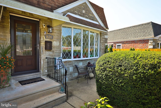 view of exterior entry featuring stone siding and a shingled roof