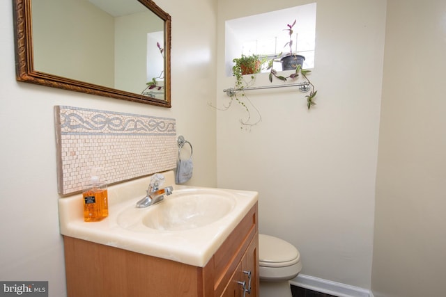 half bath with backsplash, baseboards, toilet, and vanity