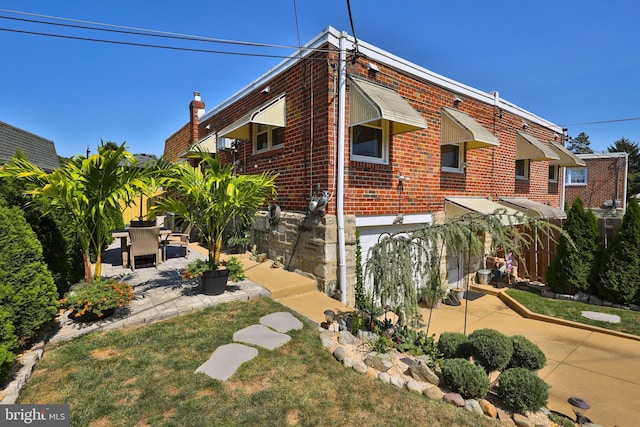 view of side of home featuring brick siding, driveway, and a patio