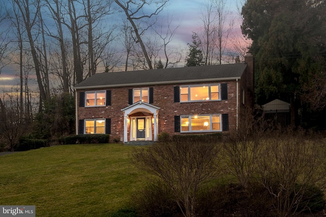 colonial-style house with brick siding, a chimney, and a front lawn