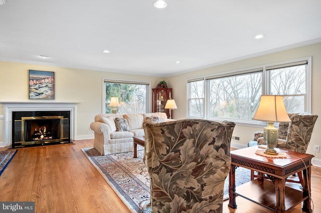 living room with wood finished floors, baseboards, recessed lighting, a glass covered fireplace, and crown molding