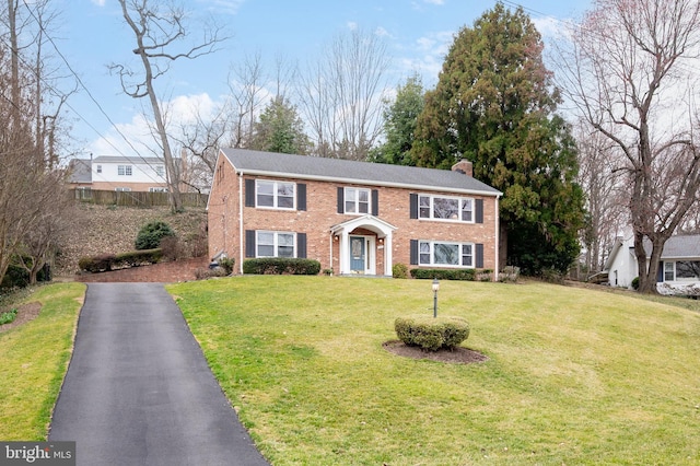 view of front of property with brick siding, driveway, a chimney, and a front lawn