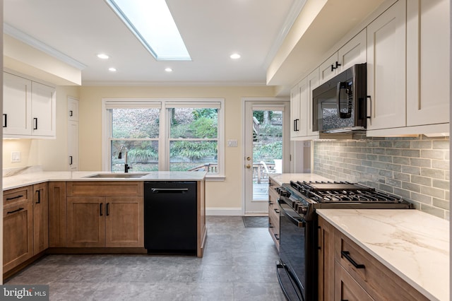 kitchen with ornamental molding, light stone counters, a skylight, black appliances, and a sink