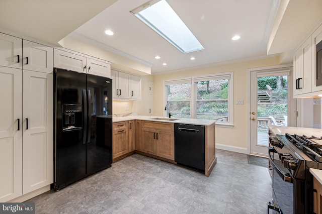 kitchen with a peninsula, a skylight, a sink, black appliances, and crown molding