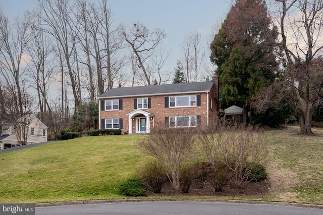 colonial-style house with brick siding, a chimney, and a front lawn