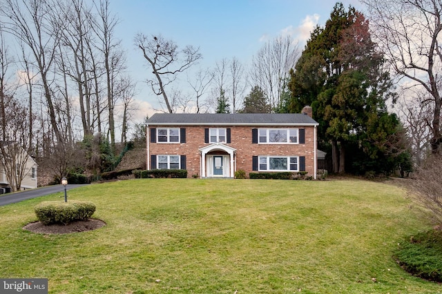 colonial home with brick siding, a front yard, and a chimney