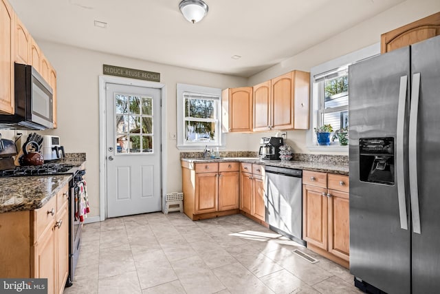 kitchen with dark stone counters, light tile patterned floors, plenty of natural light, and appliances with stainless steel finishes