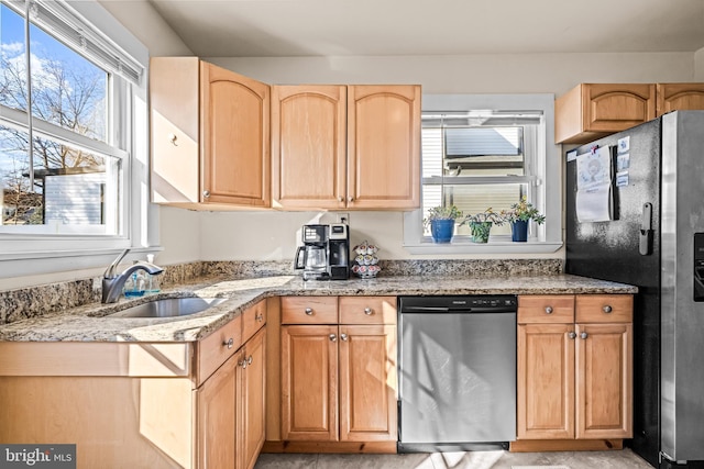 kitchen with light brown cabinets, black fridge, a sink, light stone counters, and stainless steel dishwasher