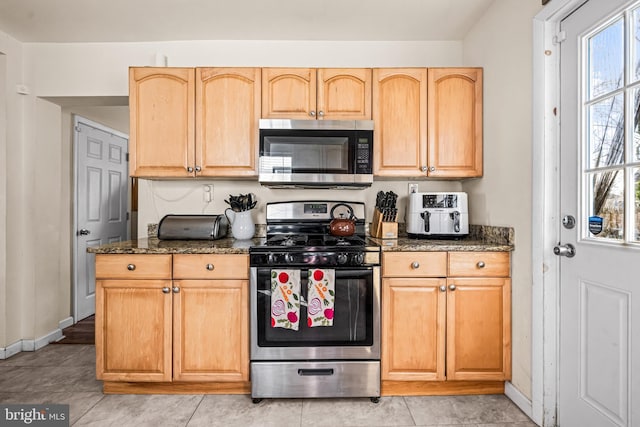 kitchen featuring dark stone countertops, stainless steel appliances, baseboards, and light brown cabinets