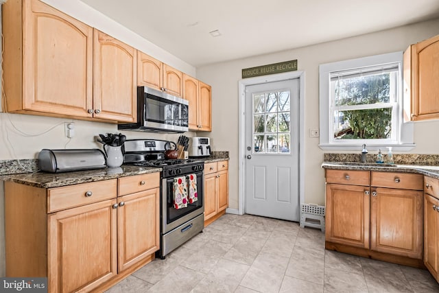 kitchen featuring light brown cabinets, appliances with stainless steel finishes, dark stone counters, and a sink