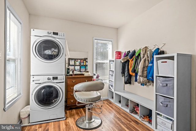 clothes washing area featuring laundry area, stacked washer and dryer, and wood finished floors