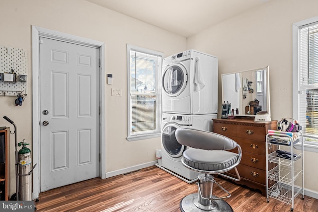 laundry area featuring laundry area, wood finished floors, baseboards, and stacked washing maching and dryer