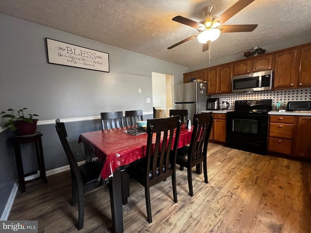 dining space featuring baseboards, a toaster, light wood-style flooring, a textured ceiling, and a ceiling fan