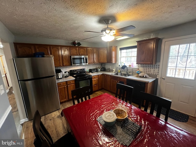 kitchen featuring a ceiling fan, a sink, black appliances, light countertops, and light wood-style floors