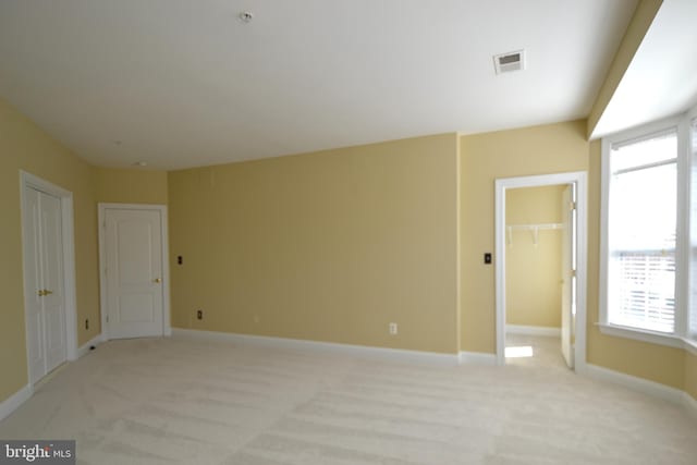 spare room with light colored carpet, baseboards, and visible vents