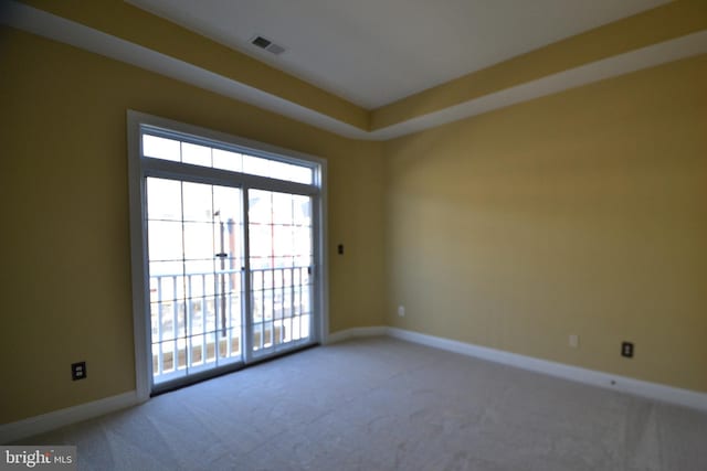 carpeted spare room featuring a tray ceiling, visible vents, and baseboards