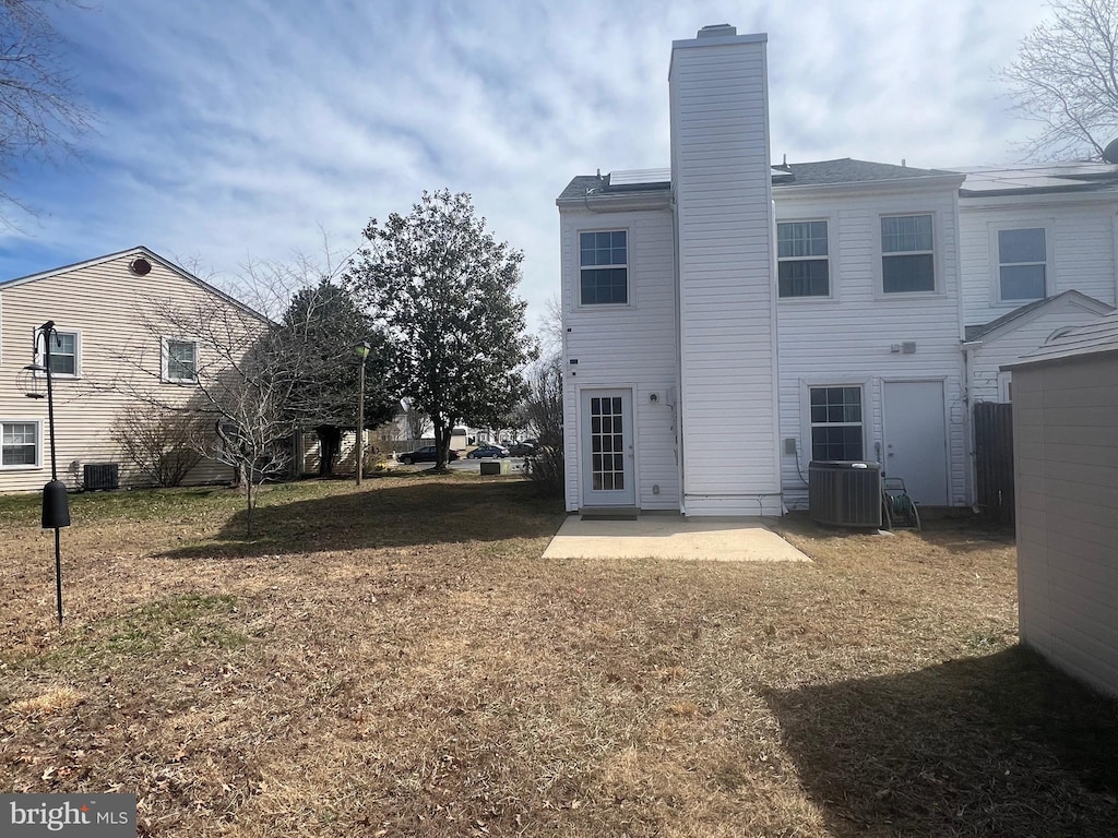 rear view of property with a patio area, a lawn, a chimney, and central AC