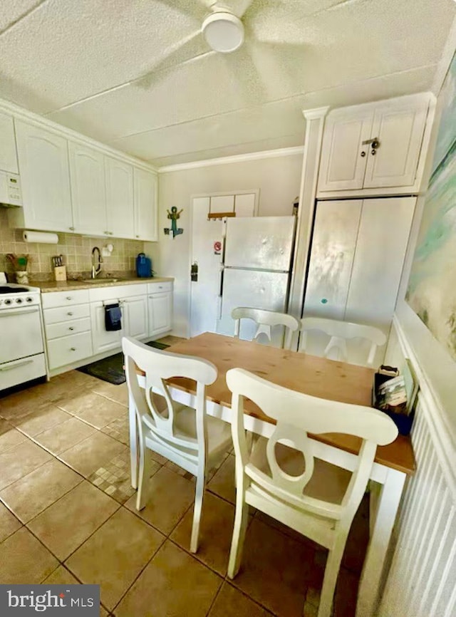 kitchen with light tile patterned floors, decorative backsplash, white cabinets, white appliances, and a sink