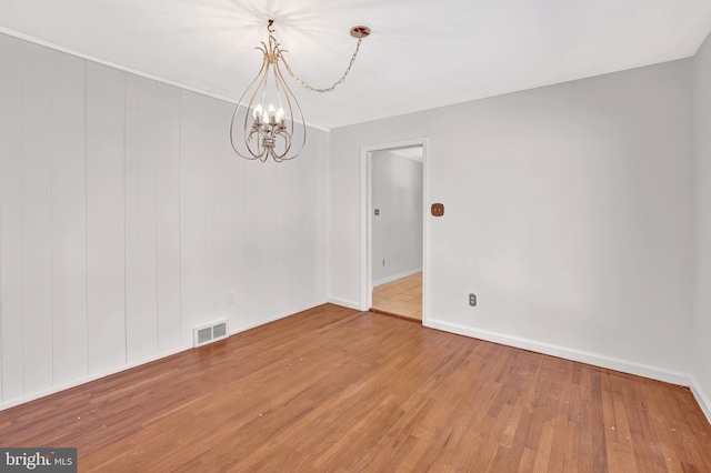 empty room featuring baseboards, wood finished floors, visible vents, and a chandelier