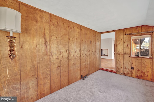 carpeted spare room featuring wood walls and vaulted ceiling