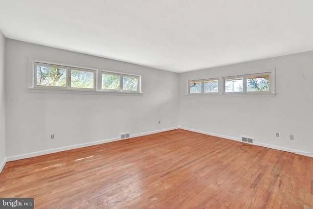 empty room featuring light wood-type flooring, visible vents, and a healthy amount of sunlight