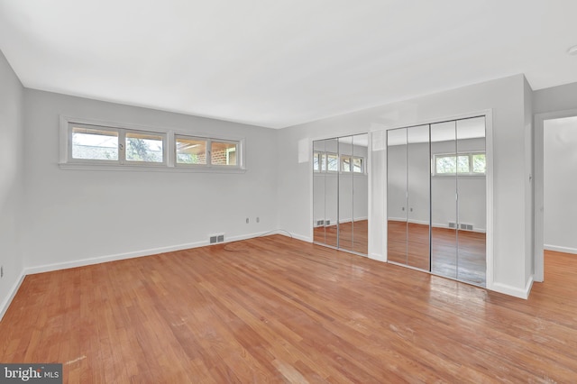 unfurnished bedroom featuring visible vents, multiple closets, and wood finished floors