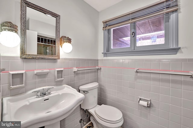 bathroom featuring tile walls, toilet, wainscoting, and a sink