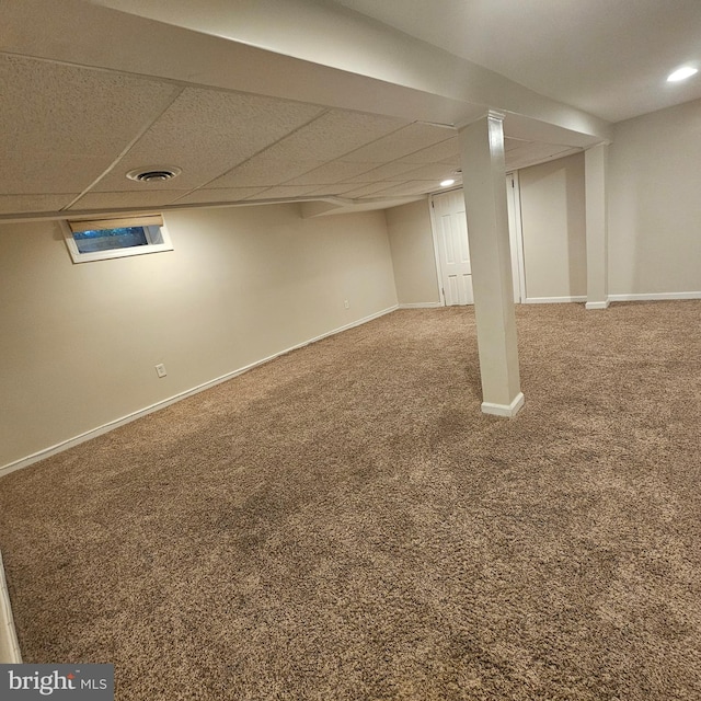 finished below grade area featuring a drop ceiling, visible vents, carpet floors, and baseboards