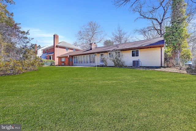 rear view of house with central air condition unit, a lawn, and a chimney