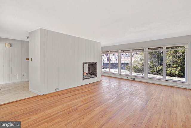 unfurnished living room featuring a multi sided fireplace, plenty of natural light, visible vents, and hardwood / wood-style flooring