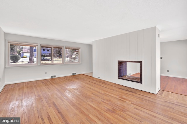 unfurnished living room featuring a multi sided fireplace, visible vents, baseboards, and wood-type flooring